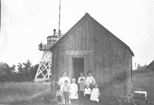 Post Office & Schoolhouse combined, circa 1898. Notice the U.S. Life-Saving Service Station lookout tower on the upper left. McMillan Township. First established on July 12, 1888 with W.L.M. Powell as its first postmaster. In 1895 the name was combined to one word Deerpark. Post Office discontinued operation on January 15, 1900; with mail service to Newberry.